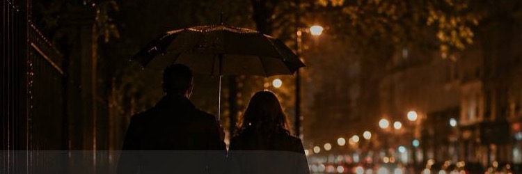 Two people under one umbrella on a rainy street at night